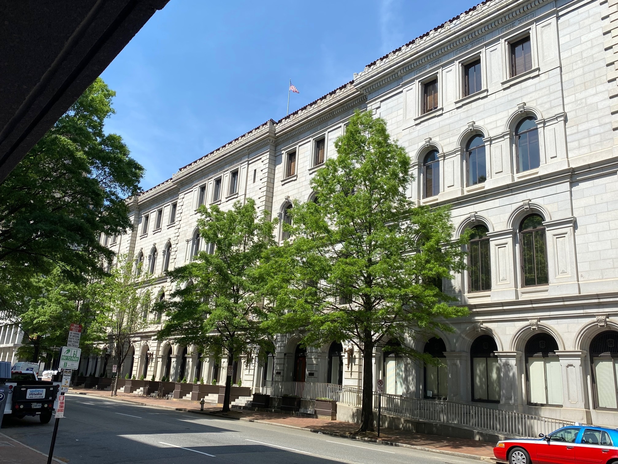 Exterior photo of the façade of the Lewis F. Powell, Jr. courthouse from the street. It's taken at an angle and shows a four story Italianate building made of white stone with two green trees in front.